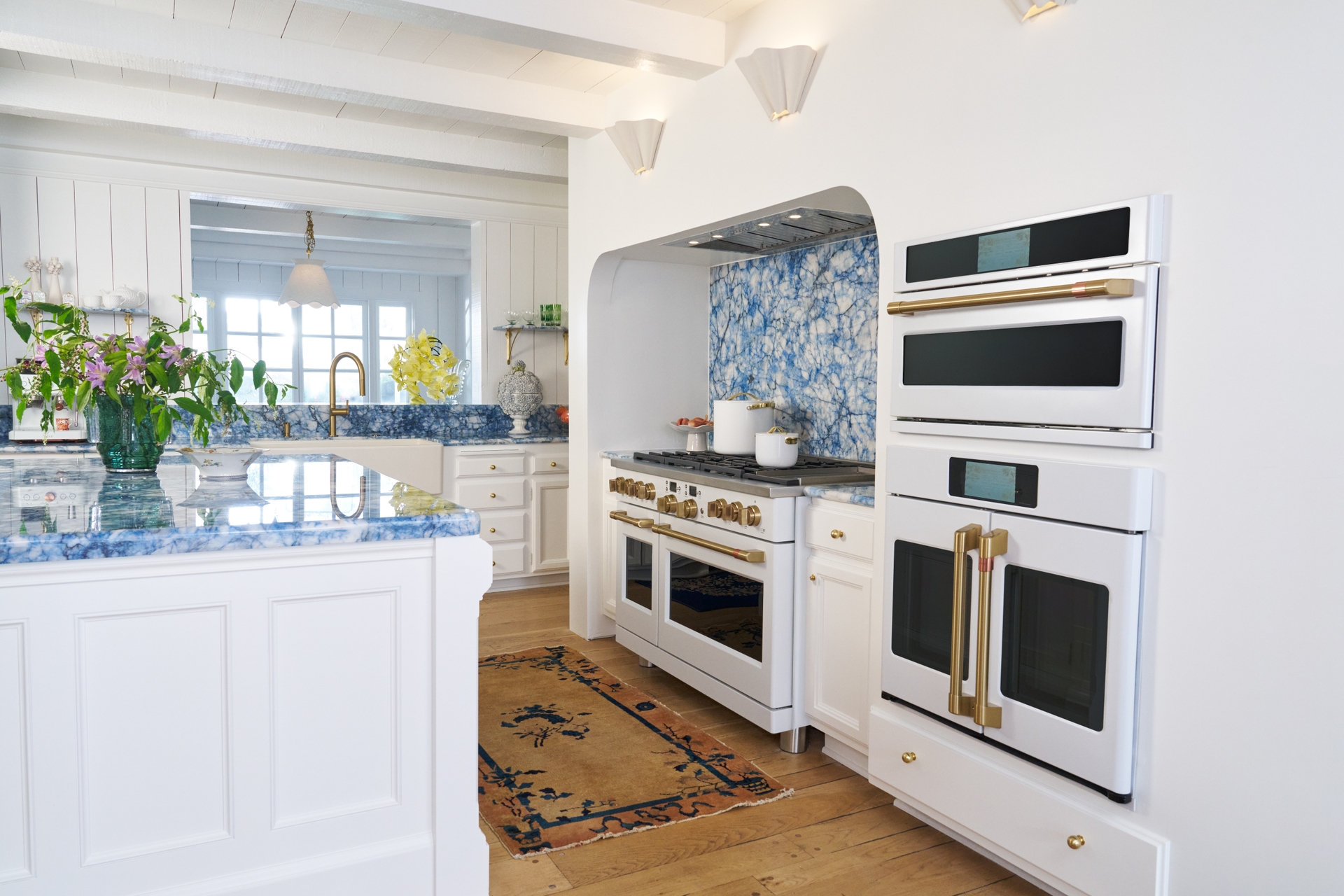  CAFÉ's Matte White appliances outfitted with Brushed Brass hardware stand out against the bold blue quartzite countertops and backsplash 
