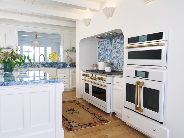  CAFÉ's Matte White appliances outfitted with Brushed Brass hardware stand out against the bold blue quartzite countertops and backsplash 