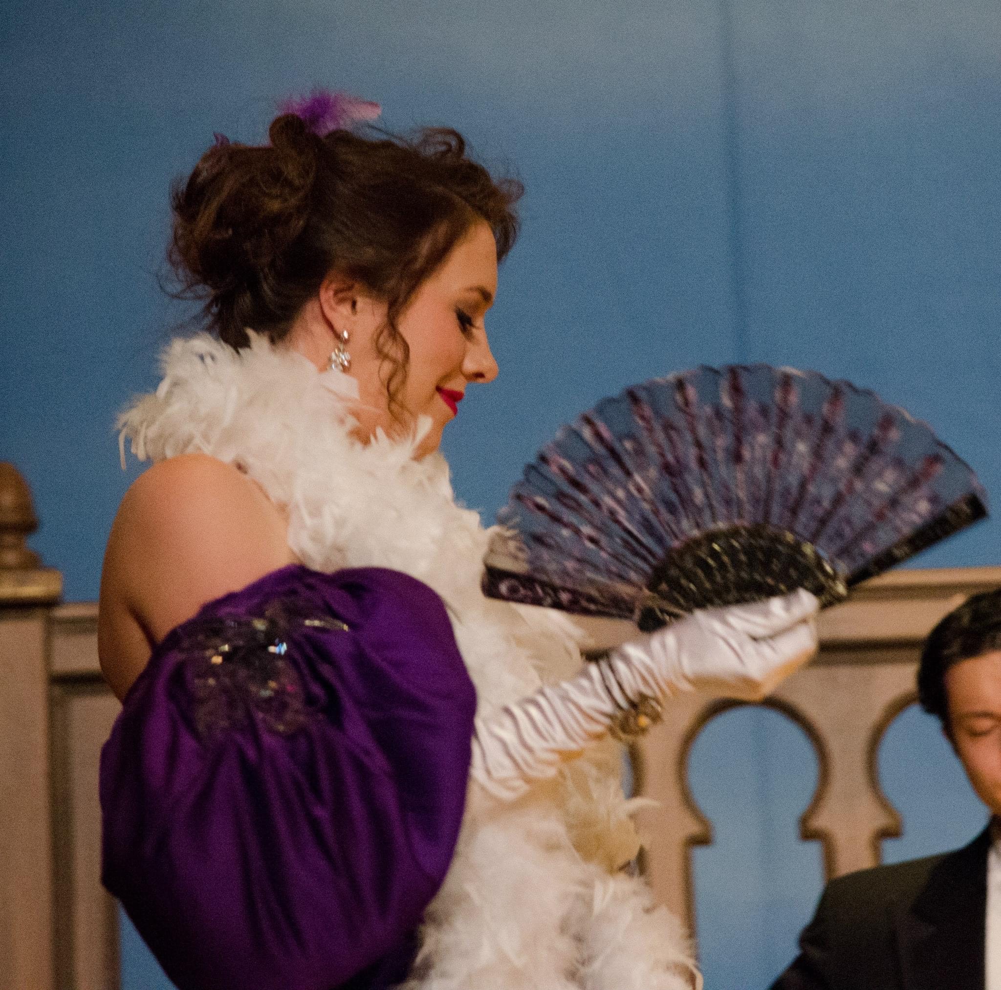 Grindatto in purple dress and feather boa portraying the character of Adele.