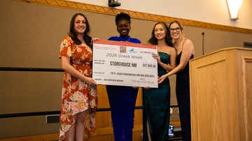 Greek Week committee members presenting the donation to the Storehouse NM representative, Danee