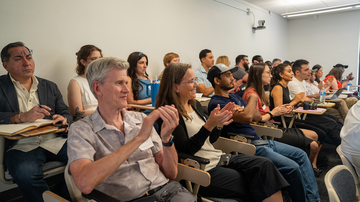 Dean Malat (second from the left first row) clapping with audience members after a presentation.