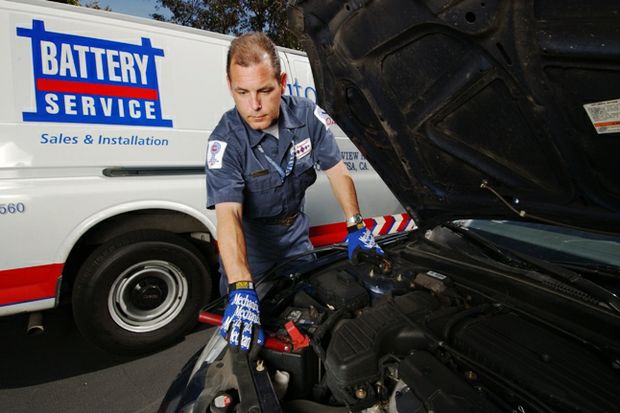 battery service tech with truck behind checks battery