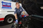battery service tech with truck behind checks battery