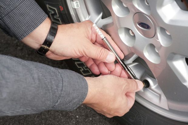 Closeup of hands using tire pressure gauge