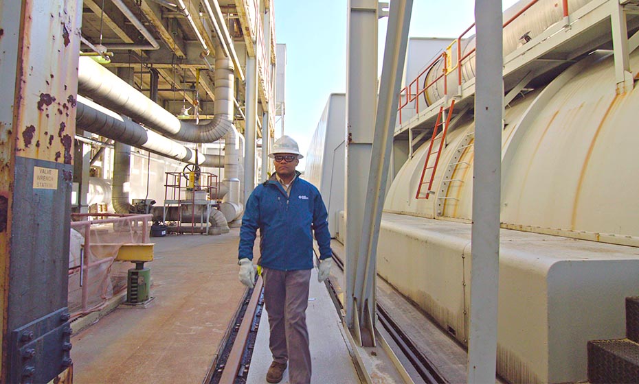 Derrick Smith, a chemistry technician at Duke Energy's Roxboro Steam Station, is pictured in front the of the plant. Smith wears a hard hat and a blue jacket.