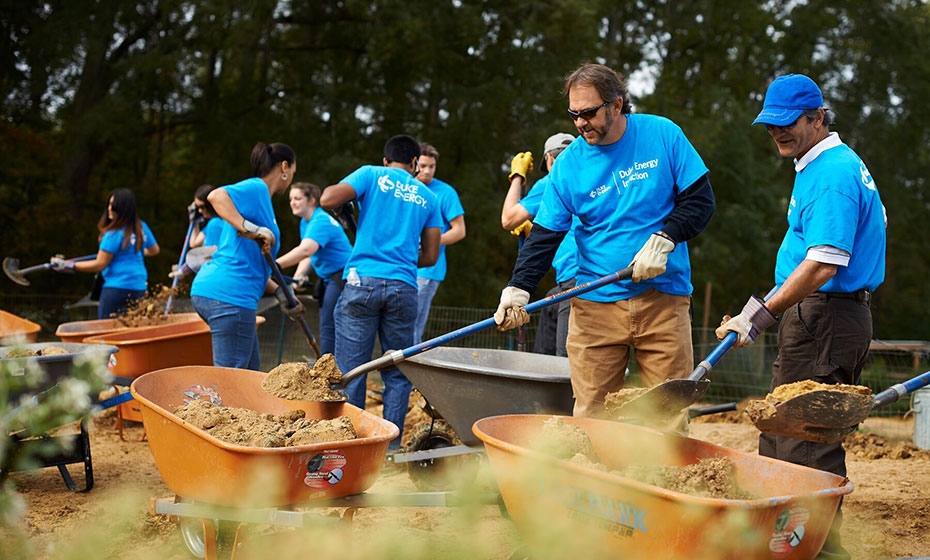 Volunteers in blue shirts move dirt from wheelbarrows to the ground at Carolina Waterfowl Rescue.