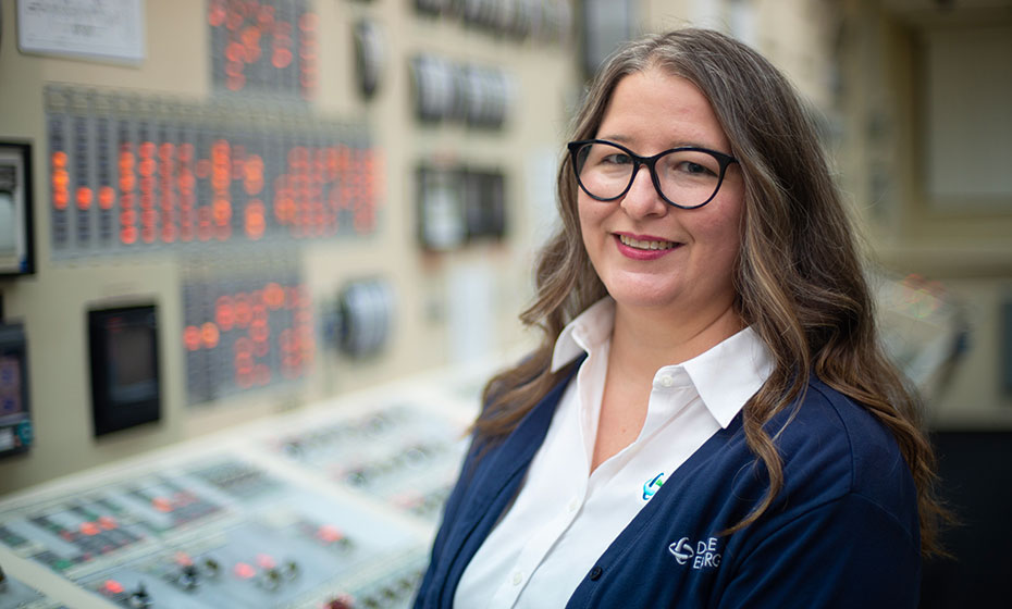 Melanie Roberts wears a crisp white shirt, a dark-colored cardigan and glasses as she stands in a control room at a Duke Energy power plant.