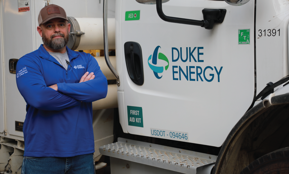 Clynt Walter standing, arms crossed, beside a Duke Energy branded bucket truck. 