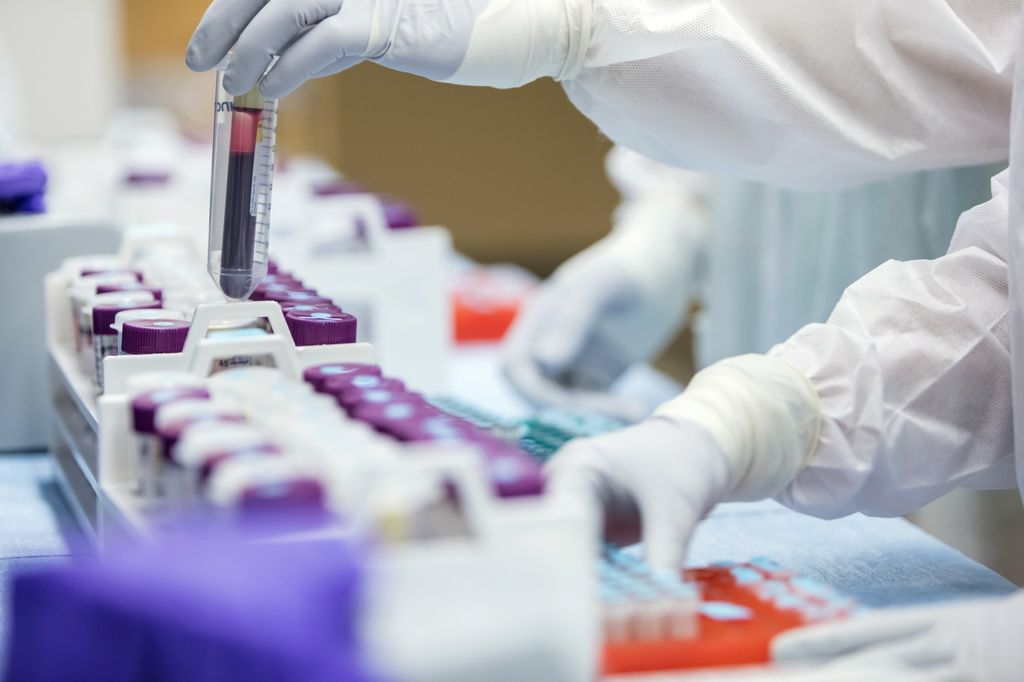 close up shot of gloved and gowned lab workers handling a vial of blood
