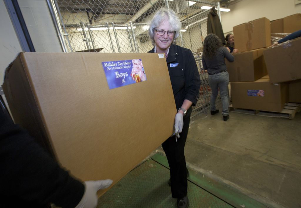 woman smiling as she helps carry a large box of donated toys