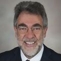 William Hersh, M.D., tiene el pelo corto, oscuro y gris, gafas, sonríe y viste un traje.