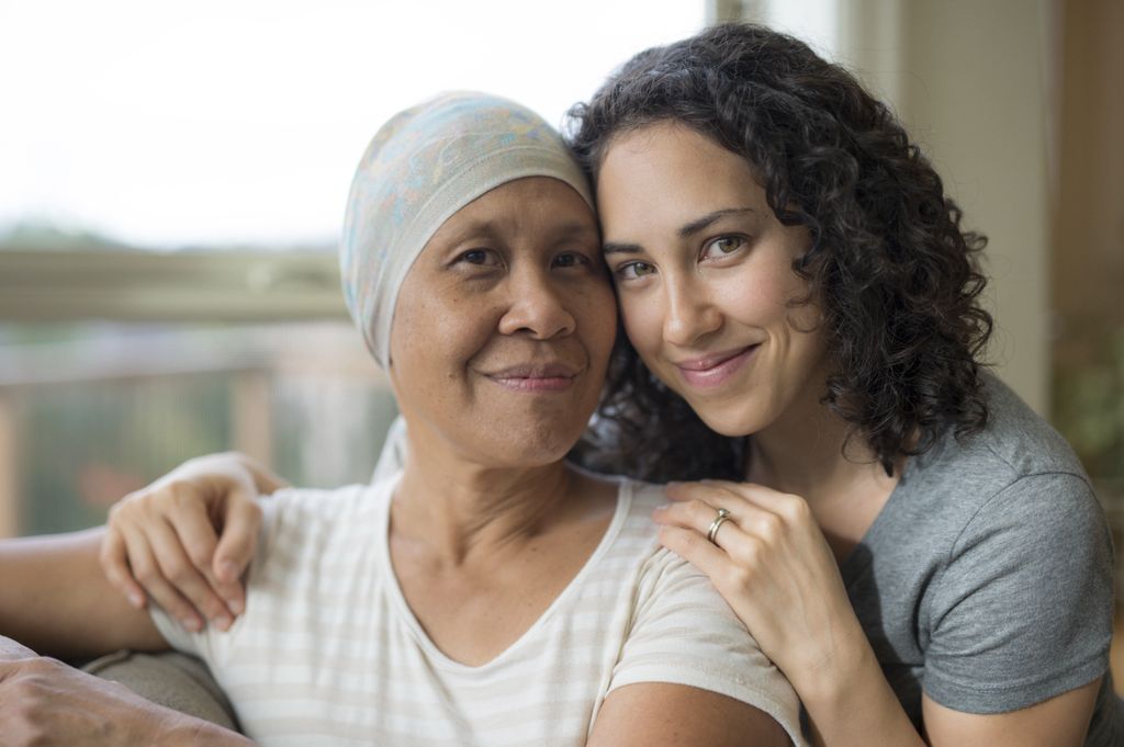 young woman with her arms around her mother. mother has cancer and her head is covered with a hat.