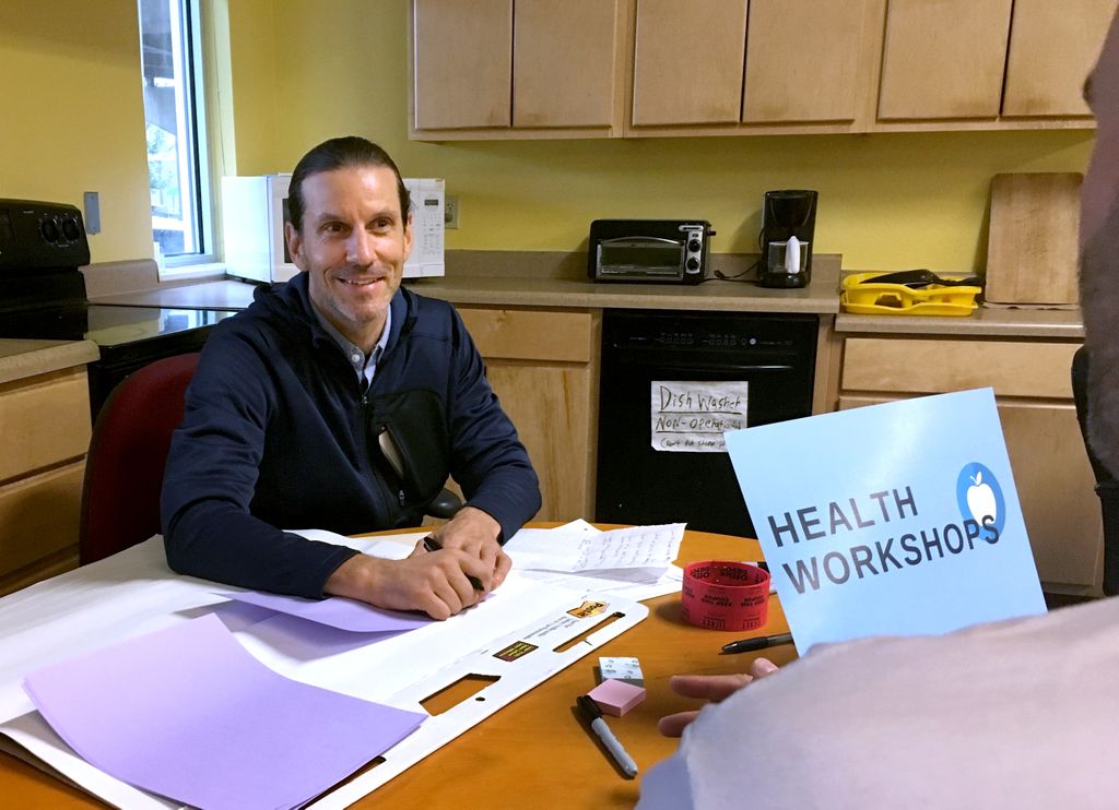 man sitting at a desk, smiling at person not seen in image
