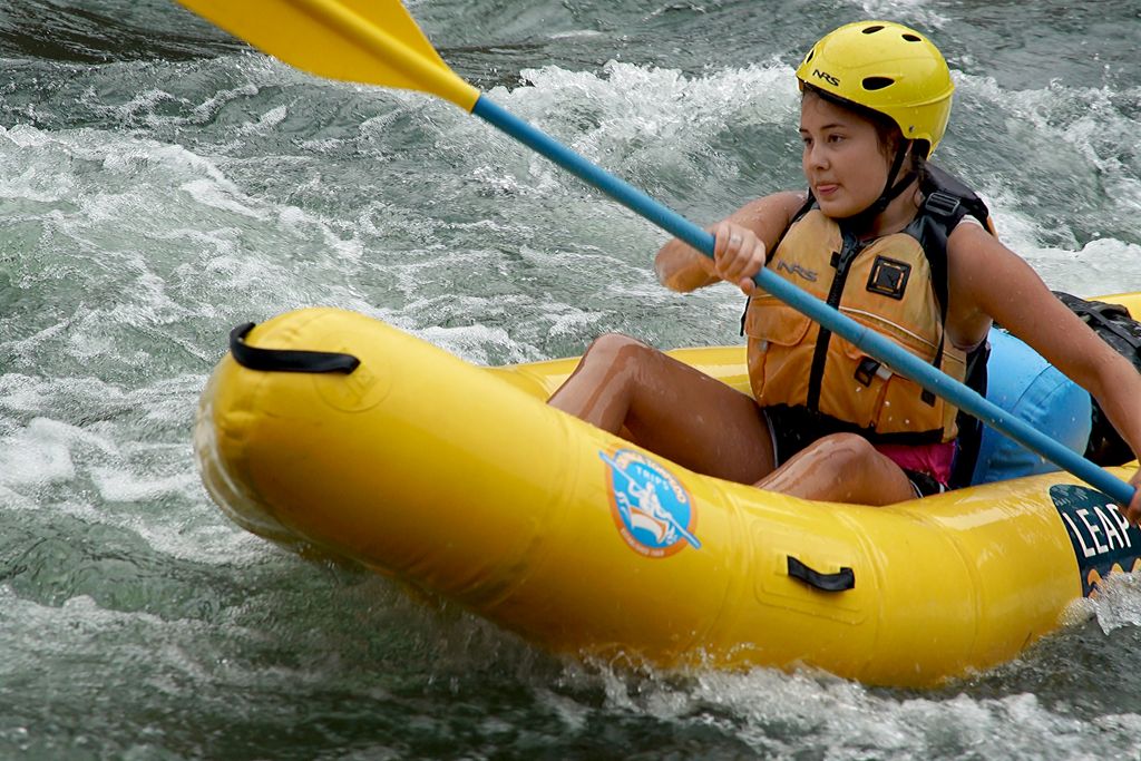 young girl paddling and inflatable kayah through whitewater rapids