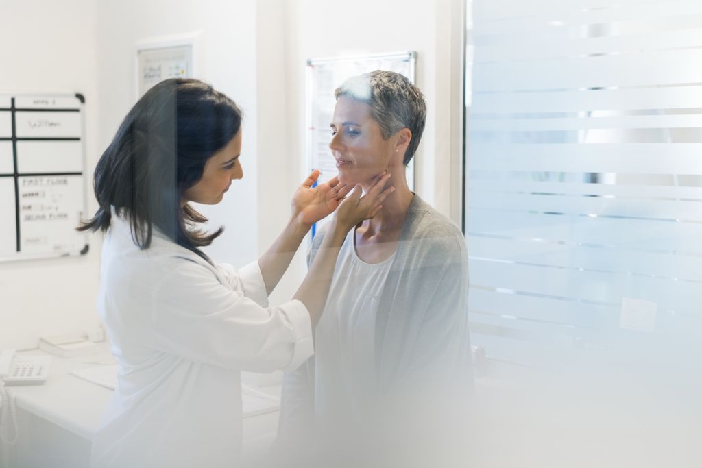 looking through window, female doctor in white lab coat examining the thyroid of a female patient