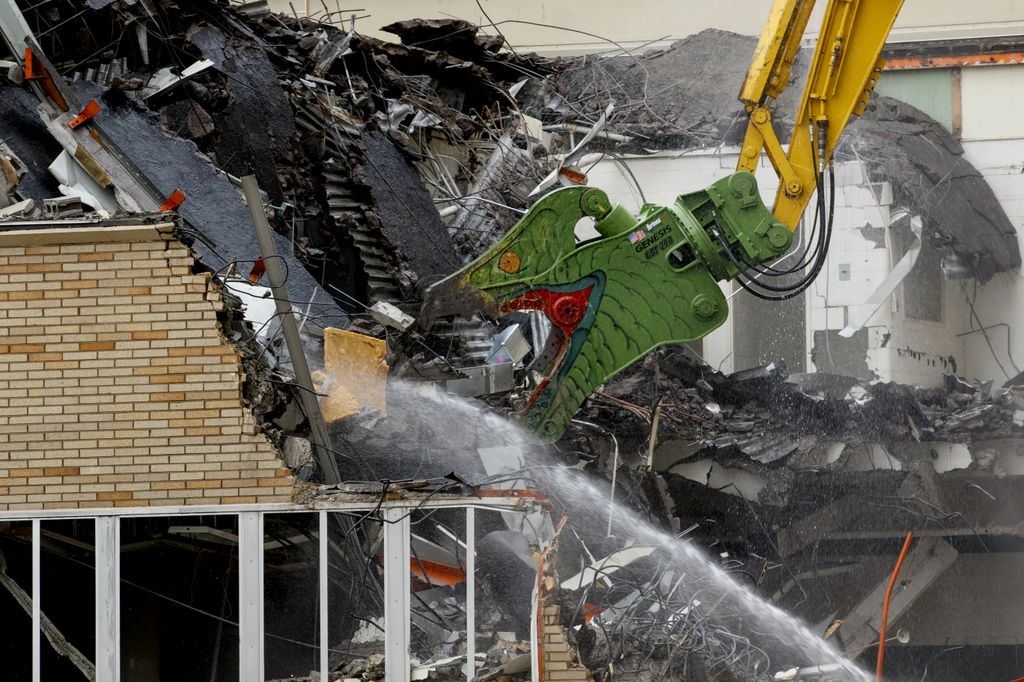 a piece of construction equipment painted to look like a dinosaur head, chomping bites out of a building