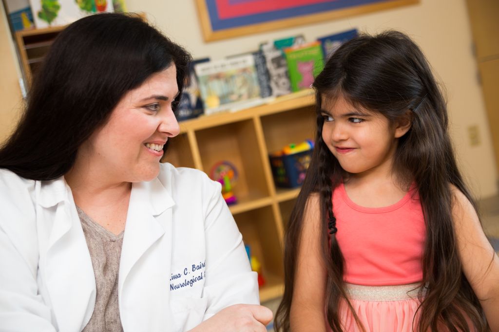 female surgeon wearing white coat, left, smiling and talking with a young girl with long dark hair