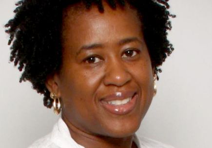 woman with dark curly hair, wearing a white shirt, smiling at camera