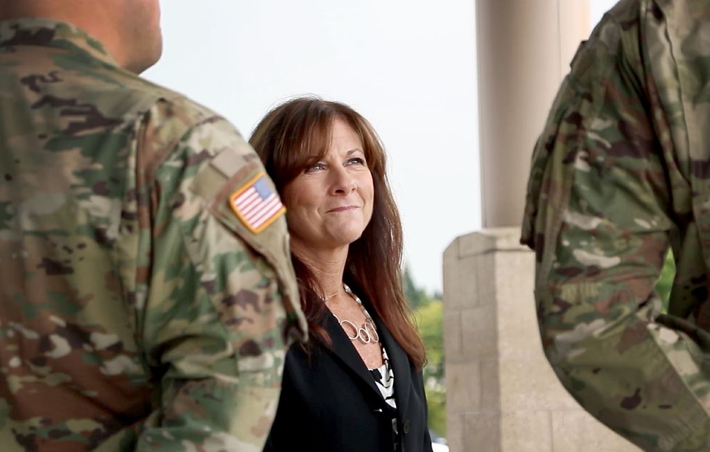 two men in fatigues, seen from the back, with leslie hammer facing the camera and smiling up at the men