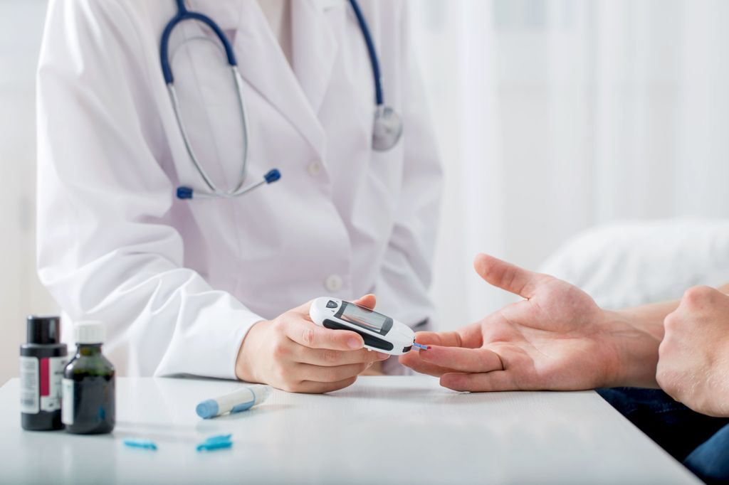  person in doctors coat shown from shoulders down, taking blood sugar measurement from a hand.