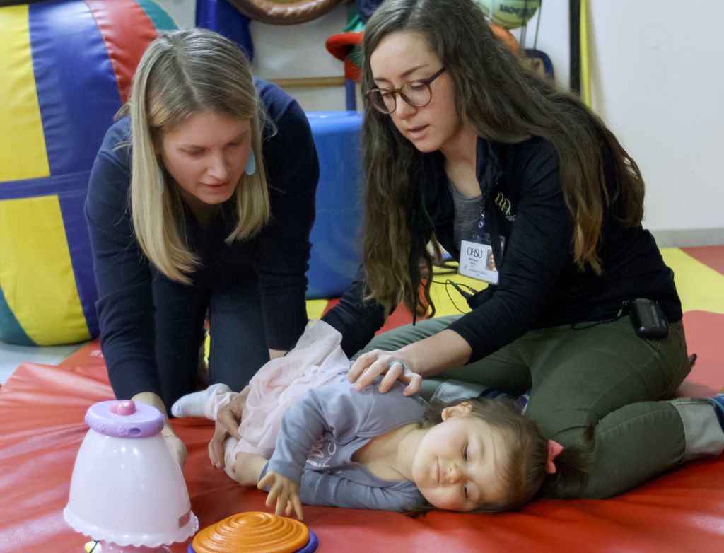 two women working with a child to learn to use an adaptive switch