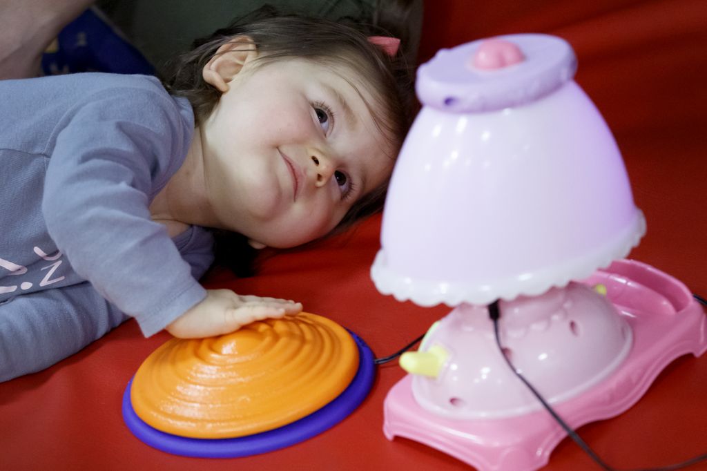 toddler lying on side, pressing a large button to turn on a toy lamp