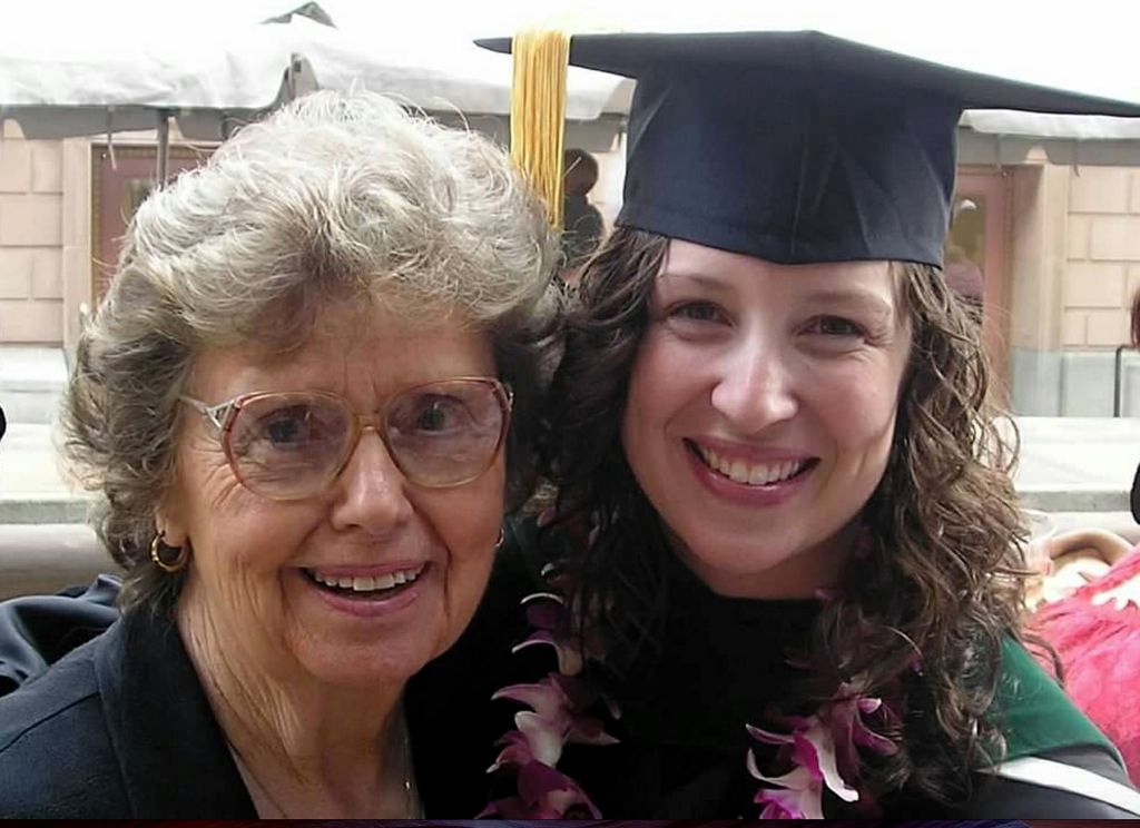 older woman with her face pressed to a younger woman's face, who is wearing a graduation cap and gown