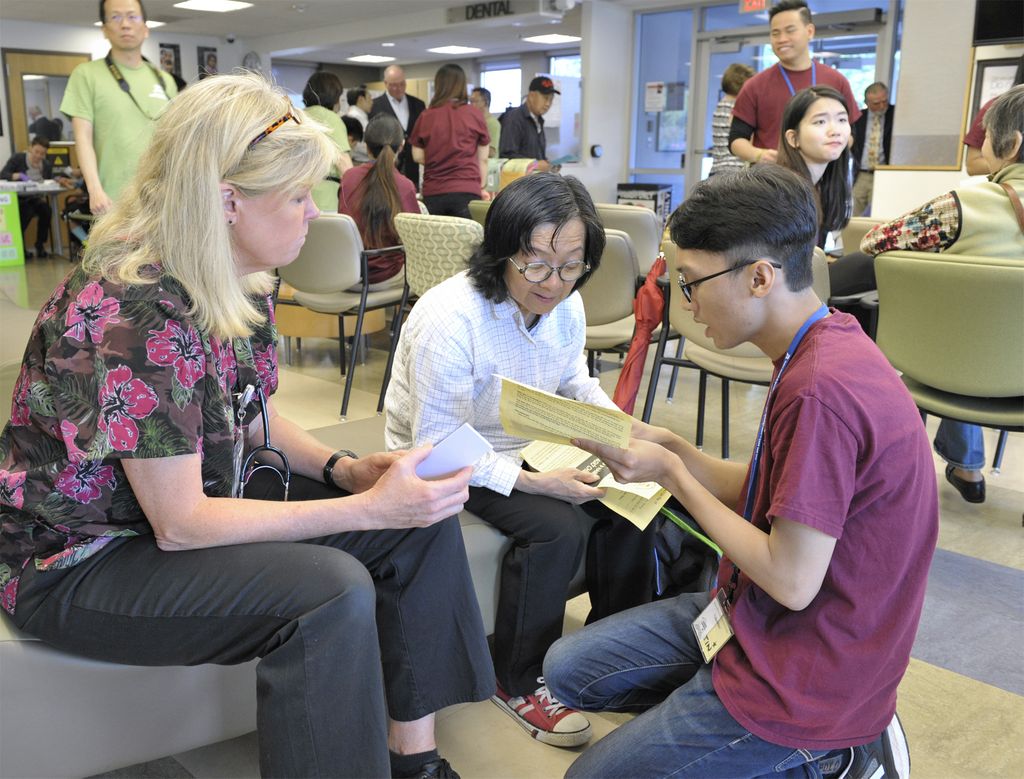 trio of people, one on his knees, translating nurse's info to a patient