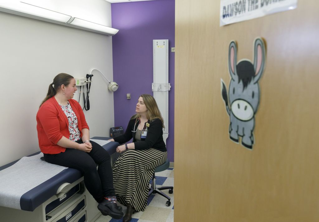 woman sitting on a hospital gurney, talking to doctor in doctor's office