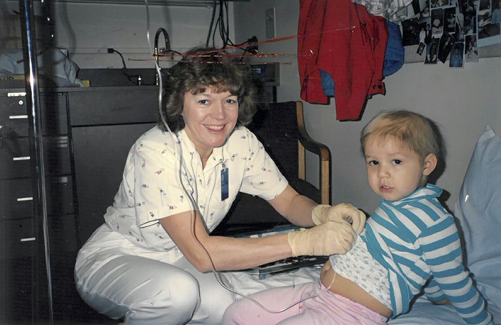 nurse squatting next to a child who is receiving treatment for leukemia