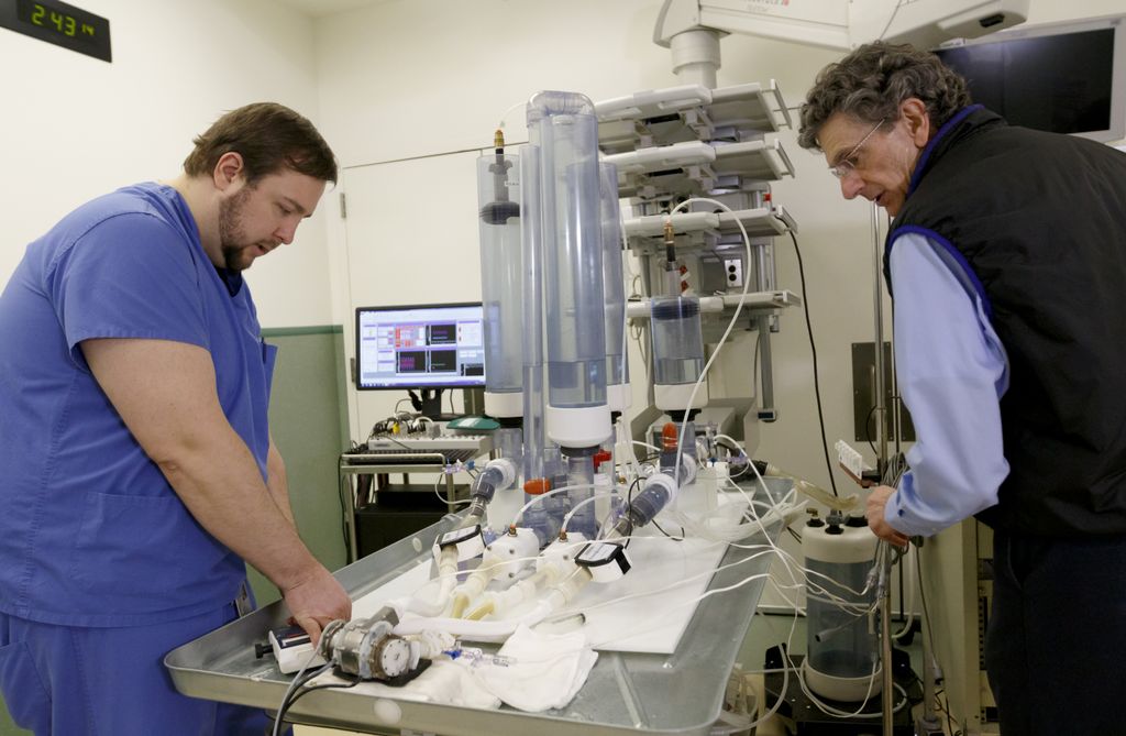 Two men on either side of a medical table, testing the output of an artificial heart