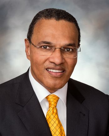 man wearing suit and site, with glasses, smiling at camera