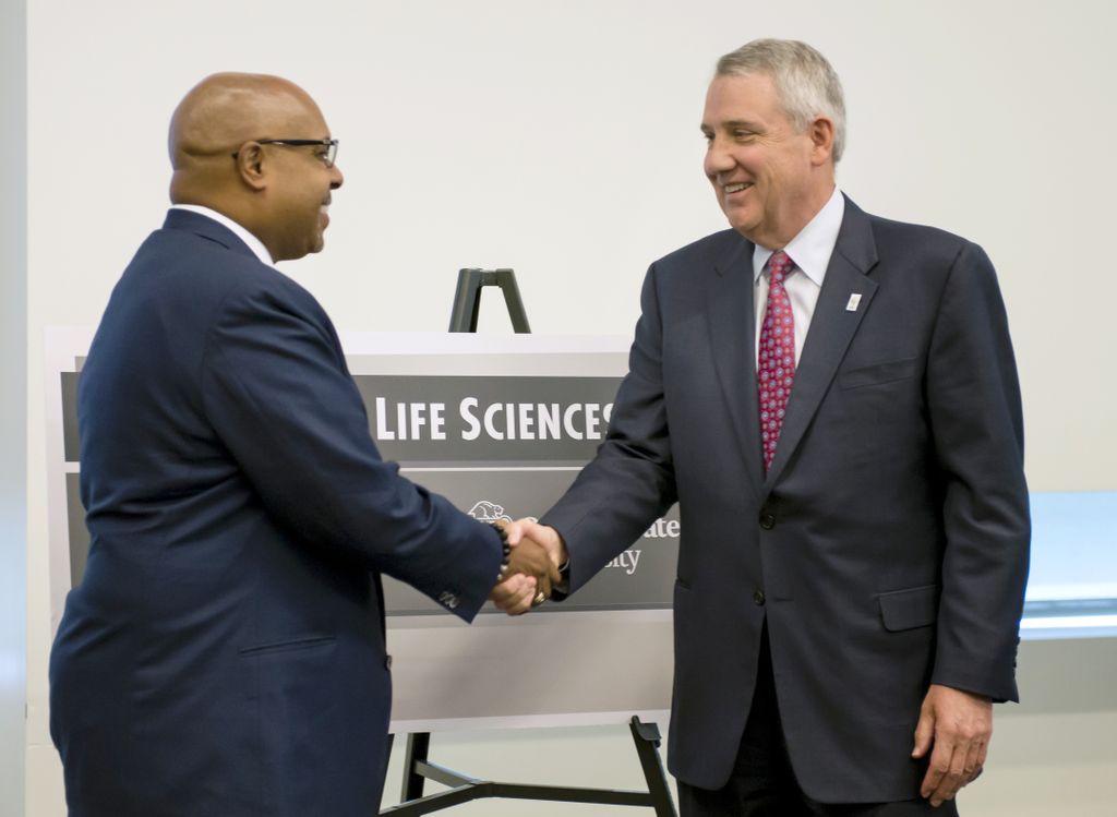 two men in suits, shaking hands in front of a sign that reads robertson life sciences building