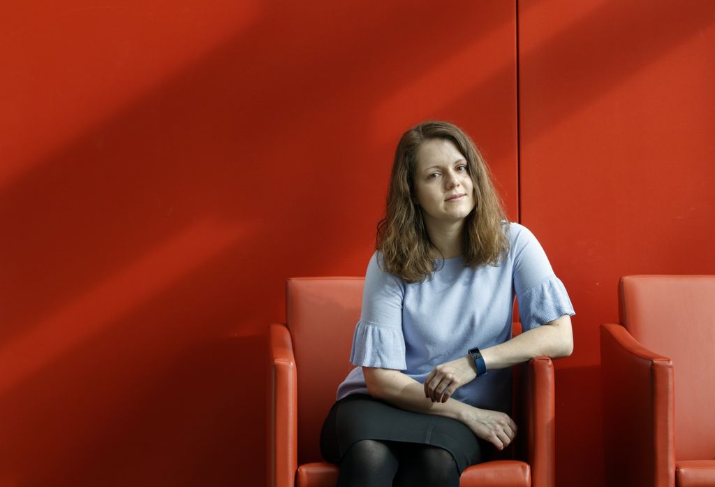 young woman sitting in a chair against a red wall, looking at camera