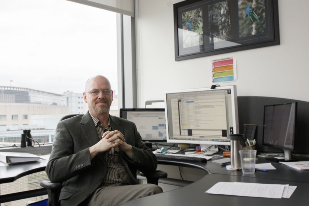 man with shaved head, sitting at his desk, looking at camera