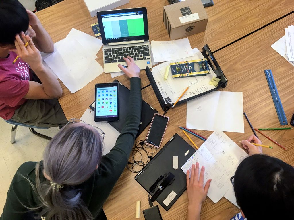 overhead shot showing students gathered around a pile of post-it notes