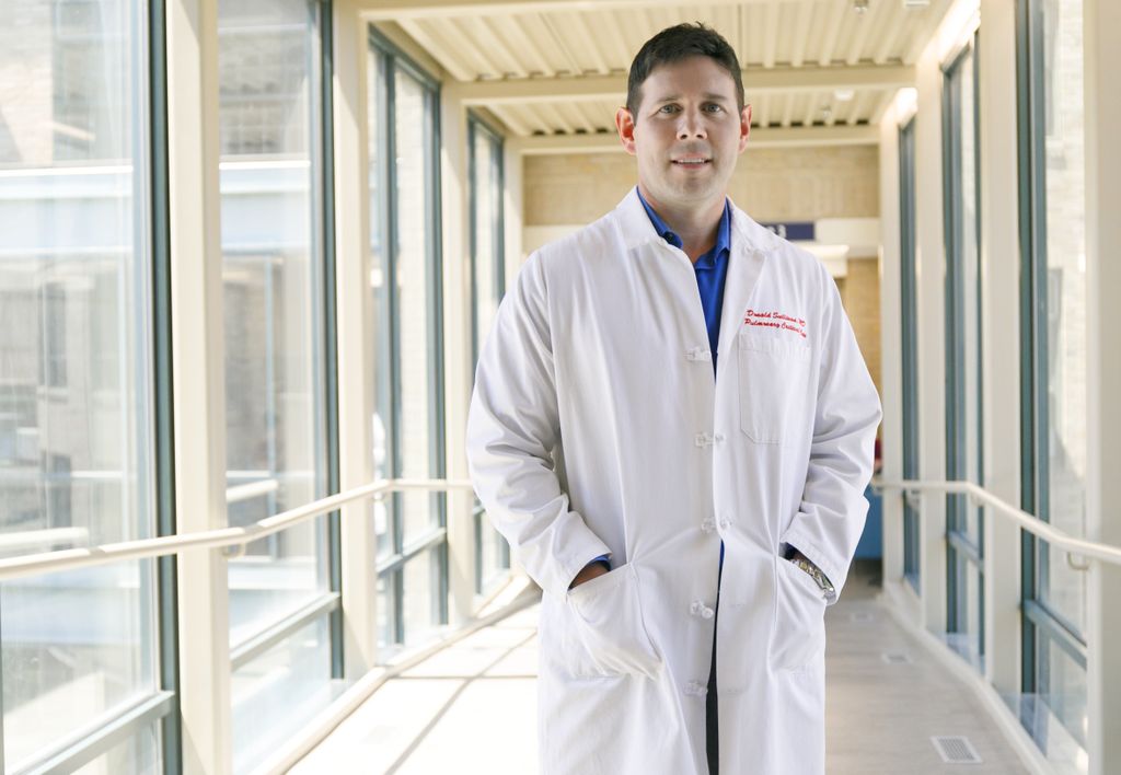 Donald Sullivan, wearing white doctor's coat, standing in a glass hallway