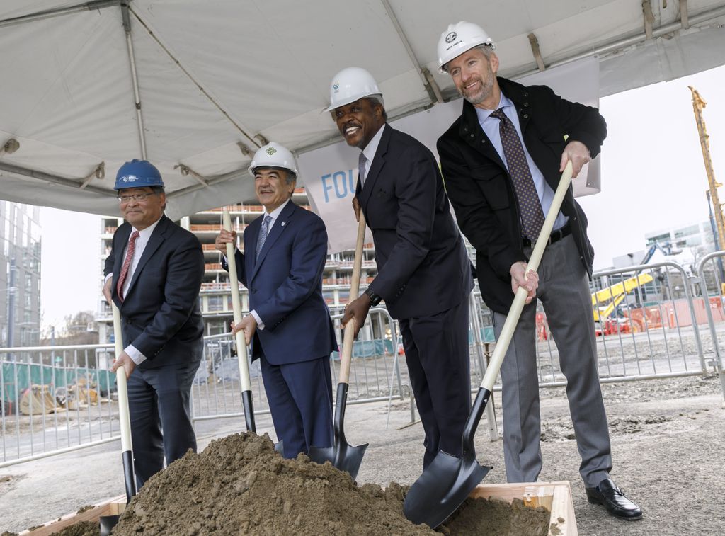 four men holding shovels, digging into dirt