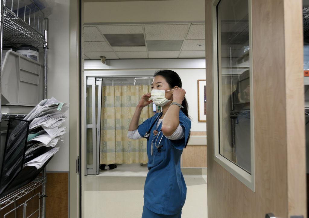 a doctor, wearing green scrubs, putting on a mask