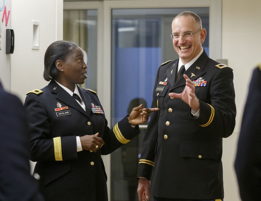 two Army personnel in uniform talk and smile with one another