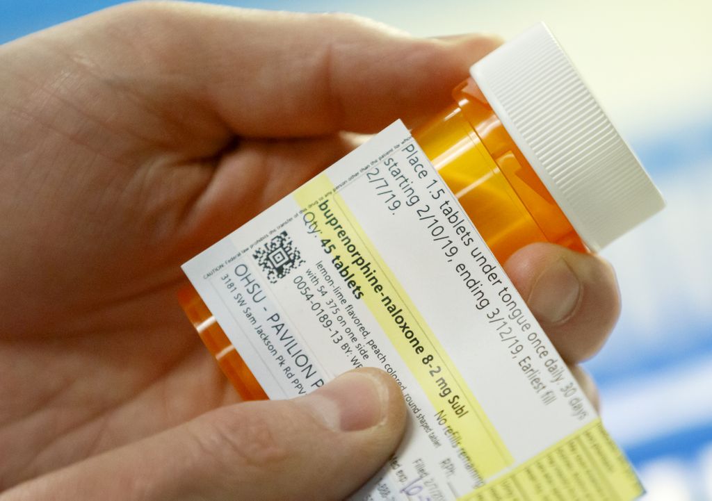 close up shot of a hand holding a prescription  bottle of buprenorphine, putting a pharmacy label on it