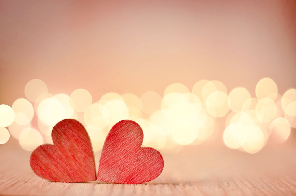 two red wooden hearts, on a table with lights in the background