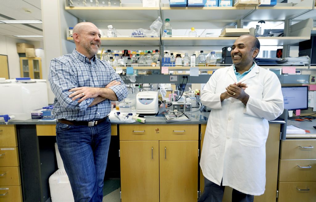 two men, leaning against a laboratory bench, talking and smiling