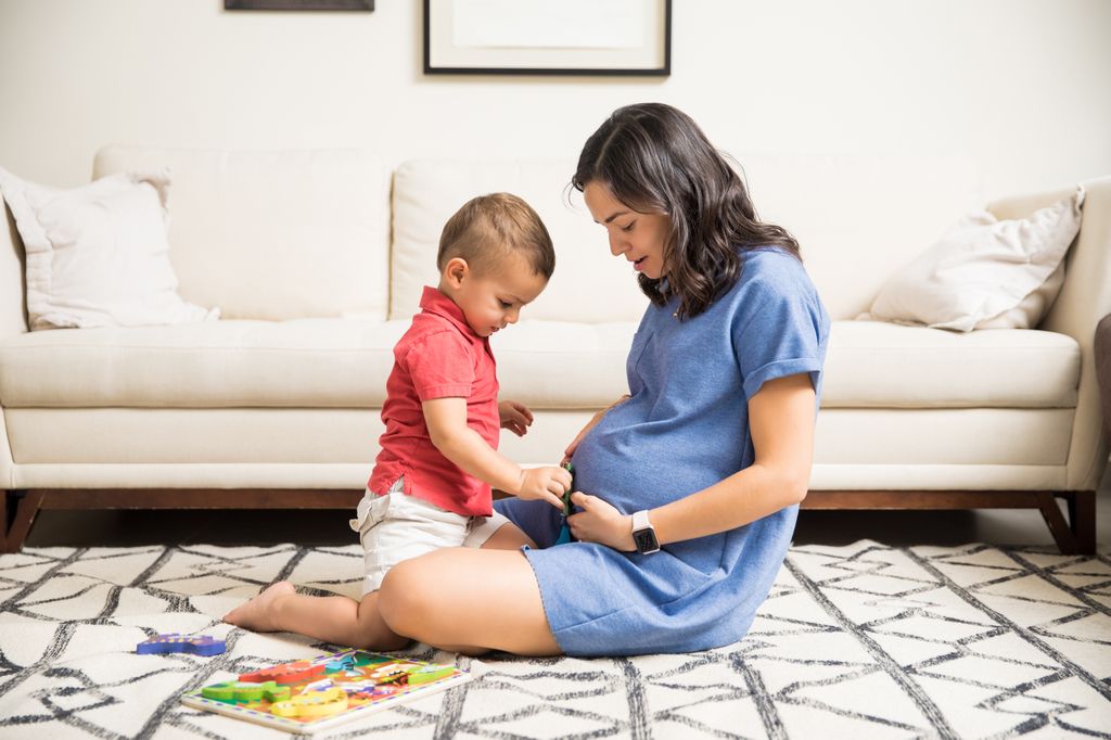Little boy playing with fetus in pregnant mother's stomach at home