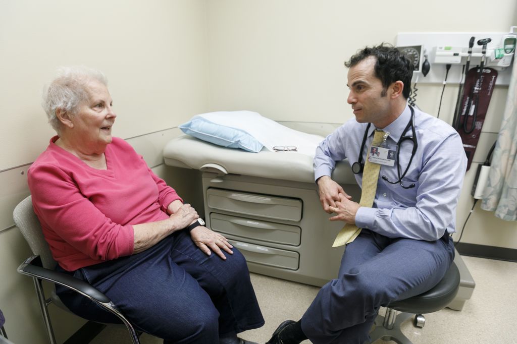 patient wearing a pink shirt on left, seated, meeting with doctor on right, seated, in a doctors office