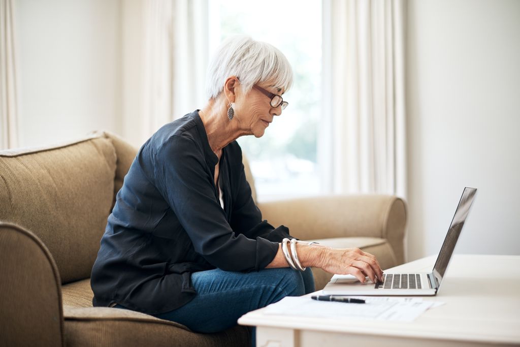 senior woman sitting on a couch, working on a laptop computer