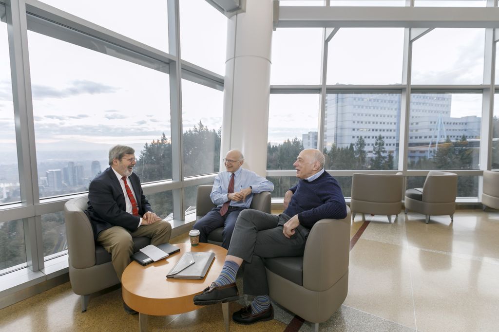 three men sitting around a table, smiling and talking