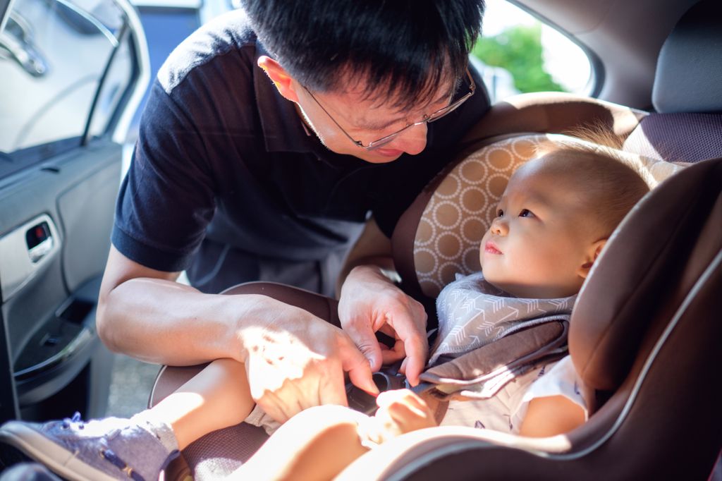 asian dad buckling an infant into a car seat