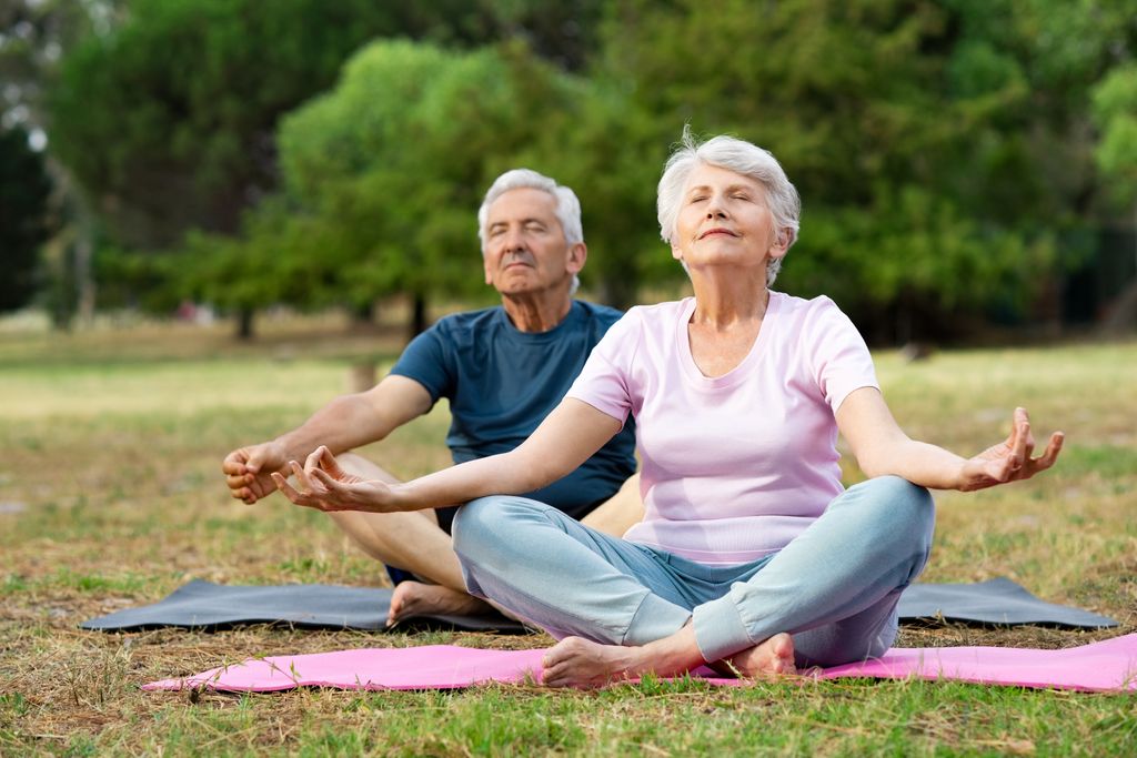senior man and woman, sitting cross legged in a field, in a mediation pose