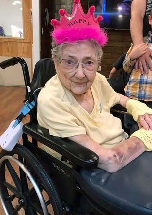 geriatric woman wearing a pink birthday hat, sitting in a wheelchair